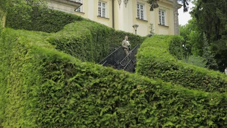 der bräutigam geht die treppe zwischen den hohen sträuchern hinunter mit einem hochzeitsbouquet an seine geliebte braut