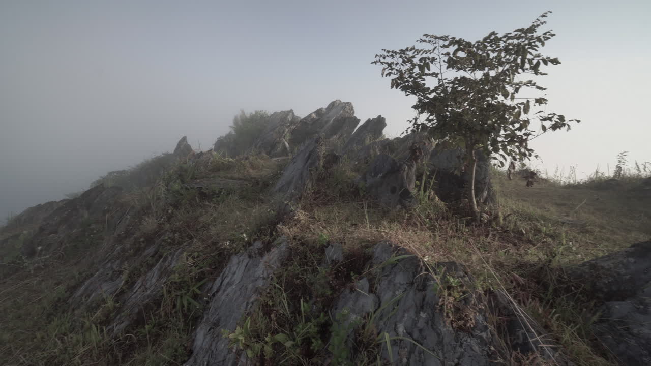 4k panorámica a la izquierda desde la cima de una montaña muy rocosa con nubes bajas y niebla en una mañana muy dramática
