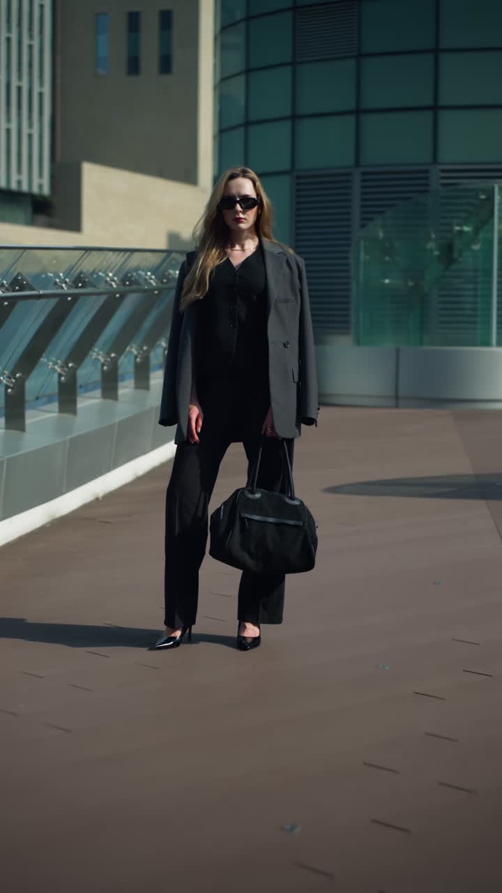Professional businesswoman in a black suit stands still on a modern office terrace as the camera dollies in from full body to close-up