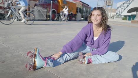 young woman in purple sweater stretching with roller skates