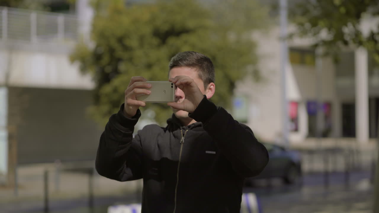 joven serio fotografiando con un teléfono inteligente en la calle