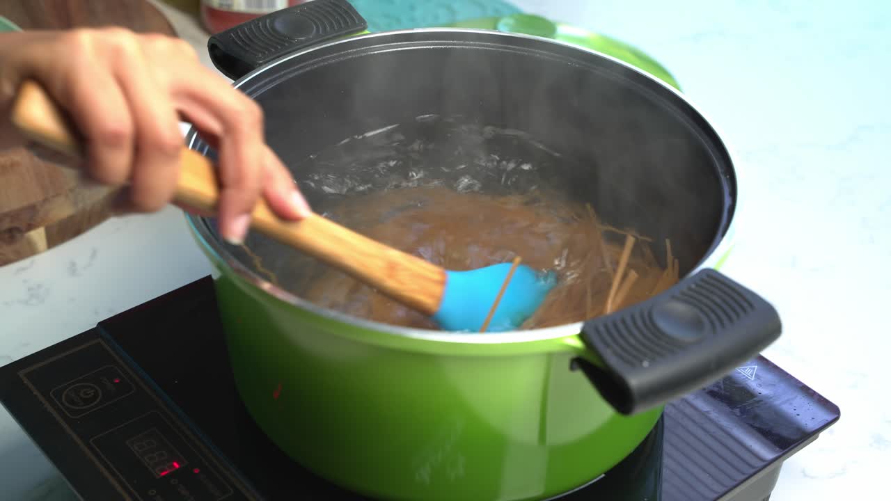 Mixing with a wooden spoon spaghetti in hot boiling water in a pot, home cooking, close up