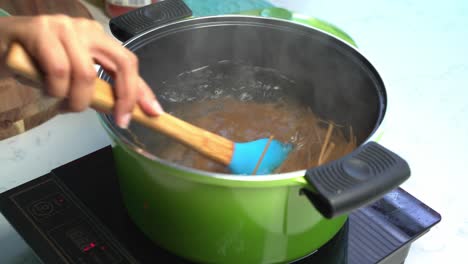 mixing with a wooden spoon spaghetti in hot boiling water in a pot, home cooking, close up