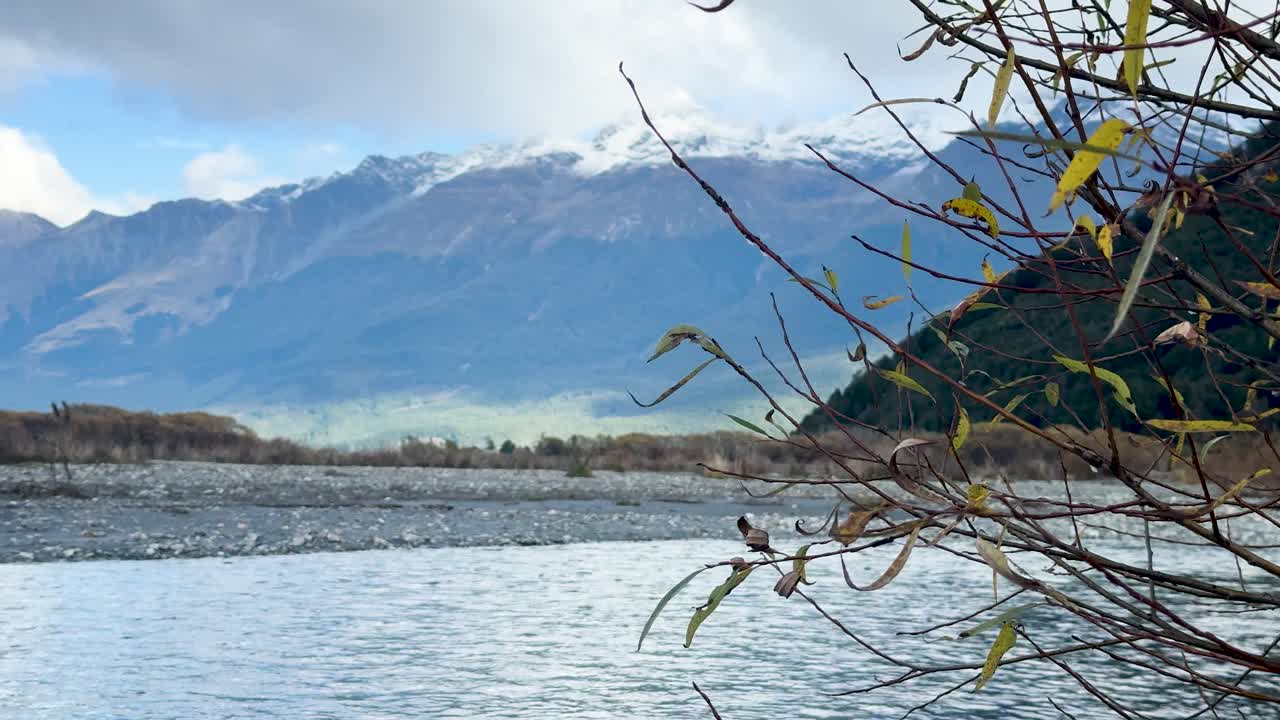 Slow pan across tranquil lakeshore, revealing distant snow-capped mountains under soft daylight