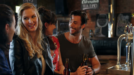 smiling group of friends interacting while having bottle of beer