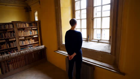 person in an old library looking out a window