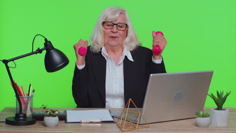 senior businesswoman working out, pumping up arm muscles lifting pink dumbbells, relaxing after work