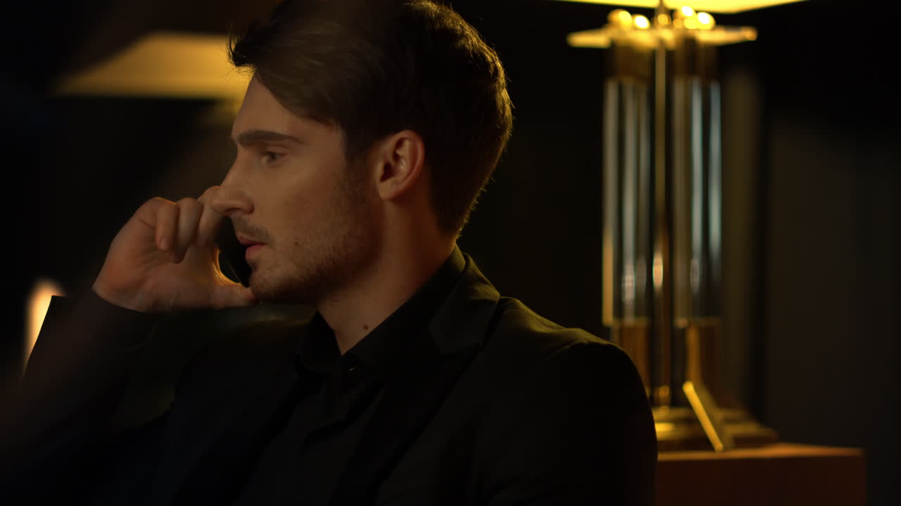 hombre ansioso hablando por teléfono móvil en un interior oscuro. jefe enfocado usando teléfono celular.