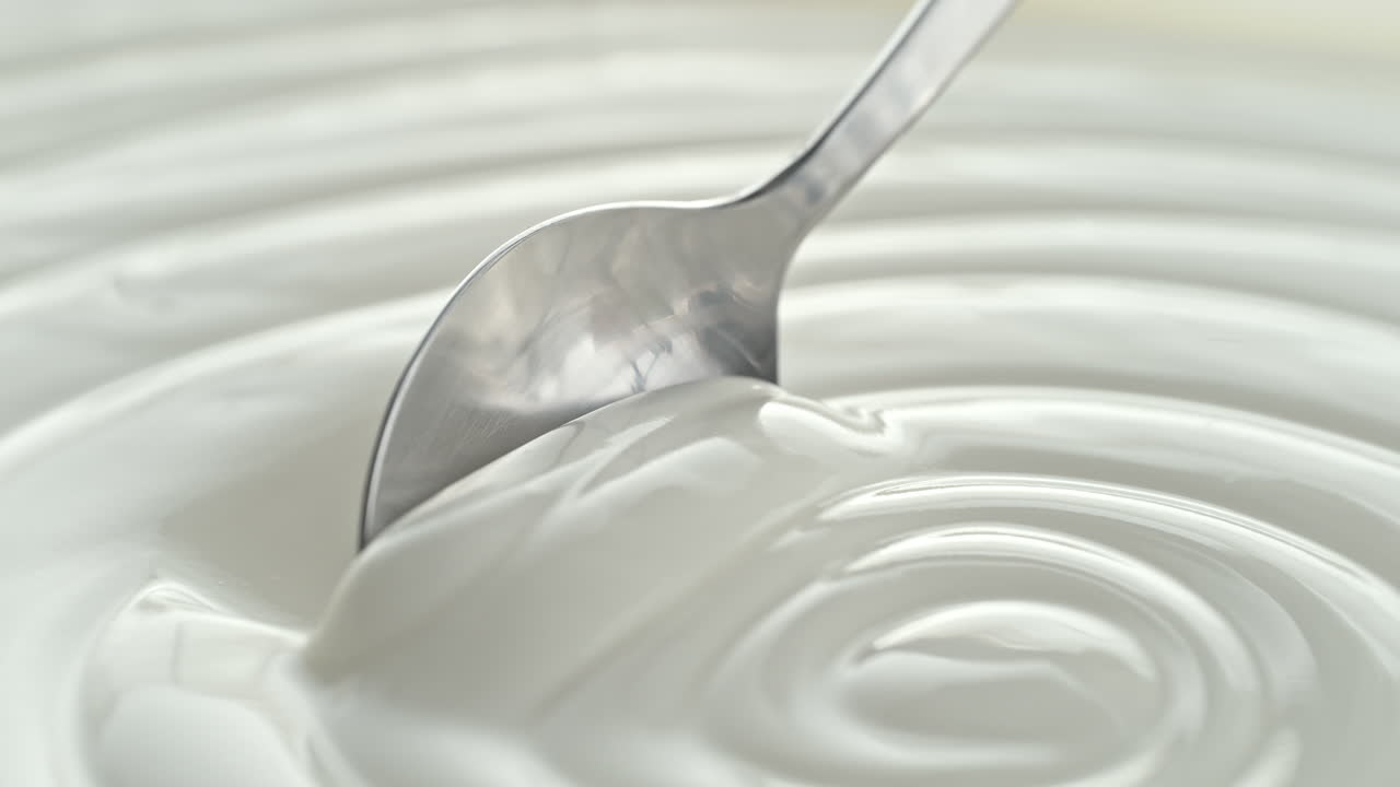 Plain Greek Yogurt Scooped with Silver Spoon from a White Bowl in Macro and Slow Motion