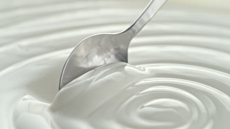 plain greek yogurt scooped with silver spoon from a white bowl in macro and slow motion