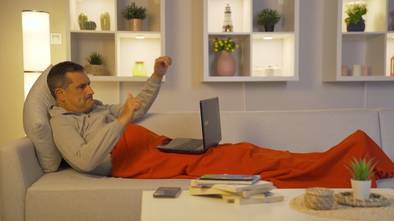 Unhappy man using laptop lying down.