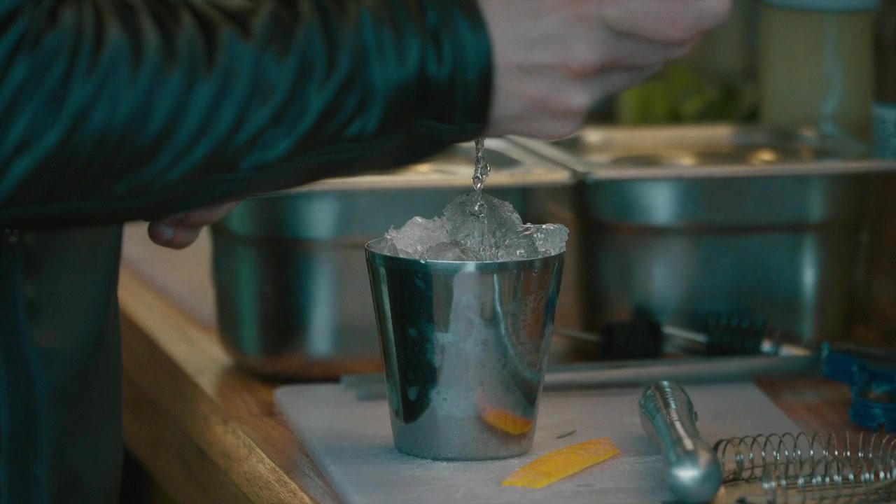 Un barista che versa alcol in cubetti di ghiaccio per cocktail.