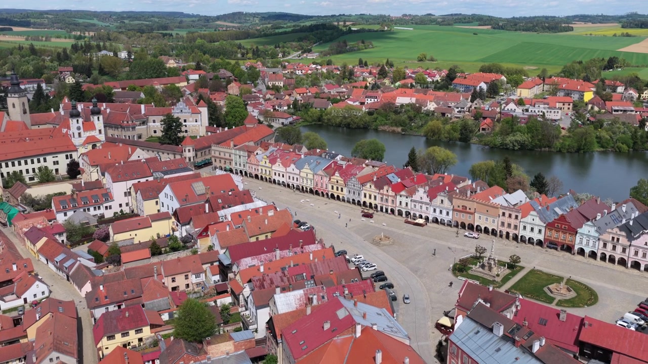 Vista aérea de drone de um complexo de castelo renascentista cercado por lagos, com uma praça histórica, torre de igreja e paisagem verde se estendendo até o horizonte, Telč, República Tcheca