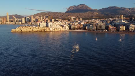 Aerial-dolly-in-towards-Benidorm-buildings-with-mountain-range-in-background-at-sunset-time