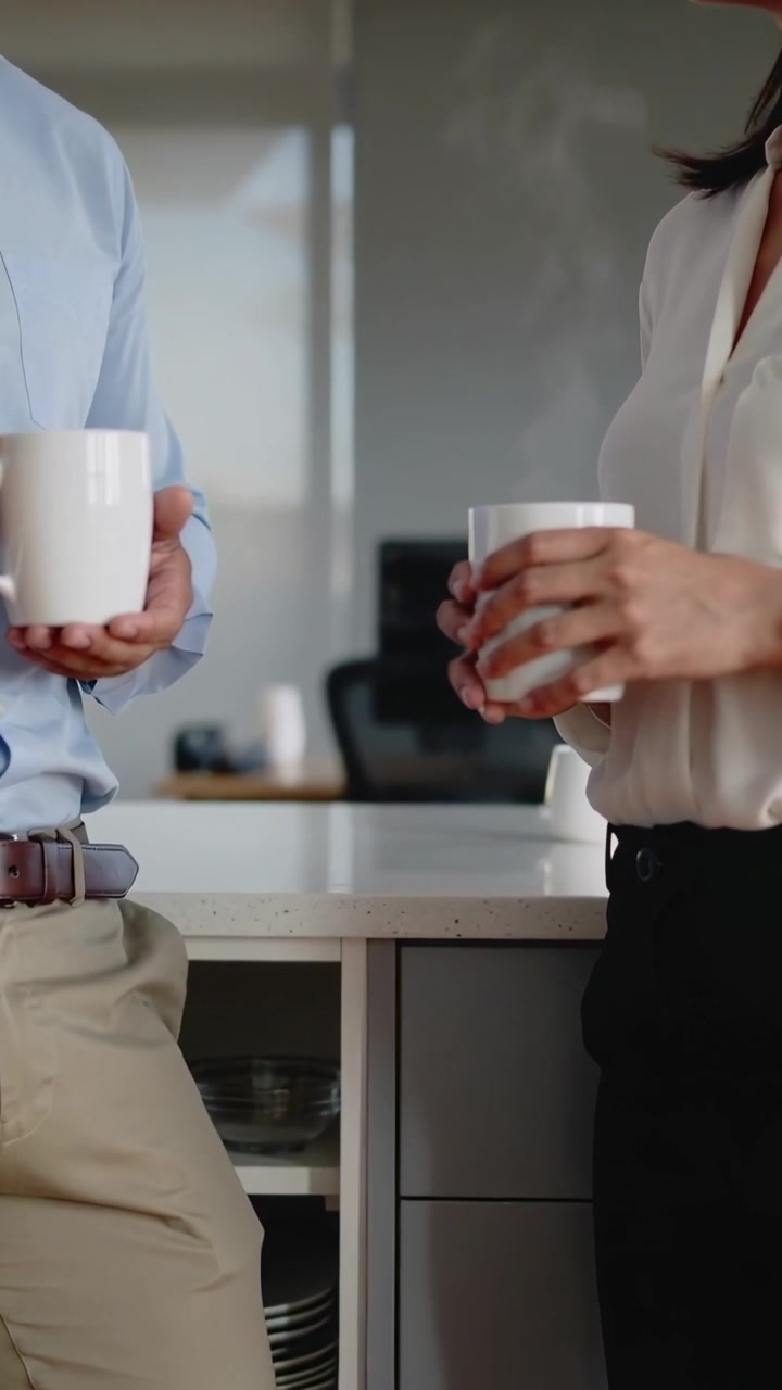 Vertikal video: Pause begynder, to medarbejdere i skjorter snakker mens de holder hvide krus på kontoret