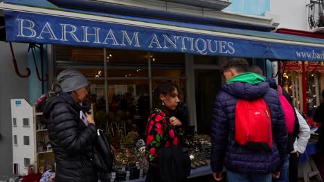 tourists view antiques for sale in a shop at portobello road market, notting hill. slowmo
