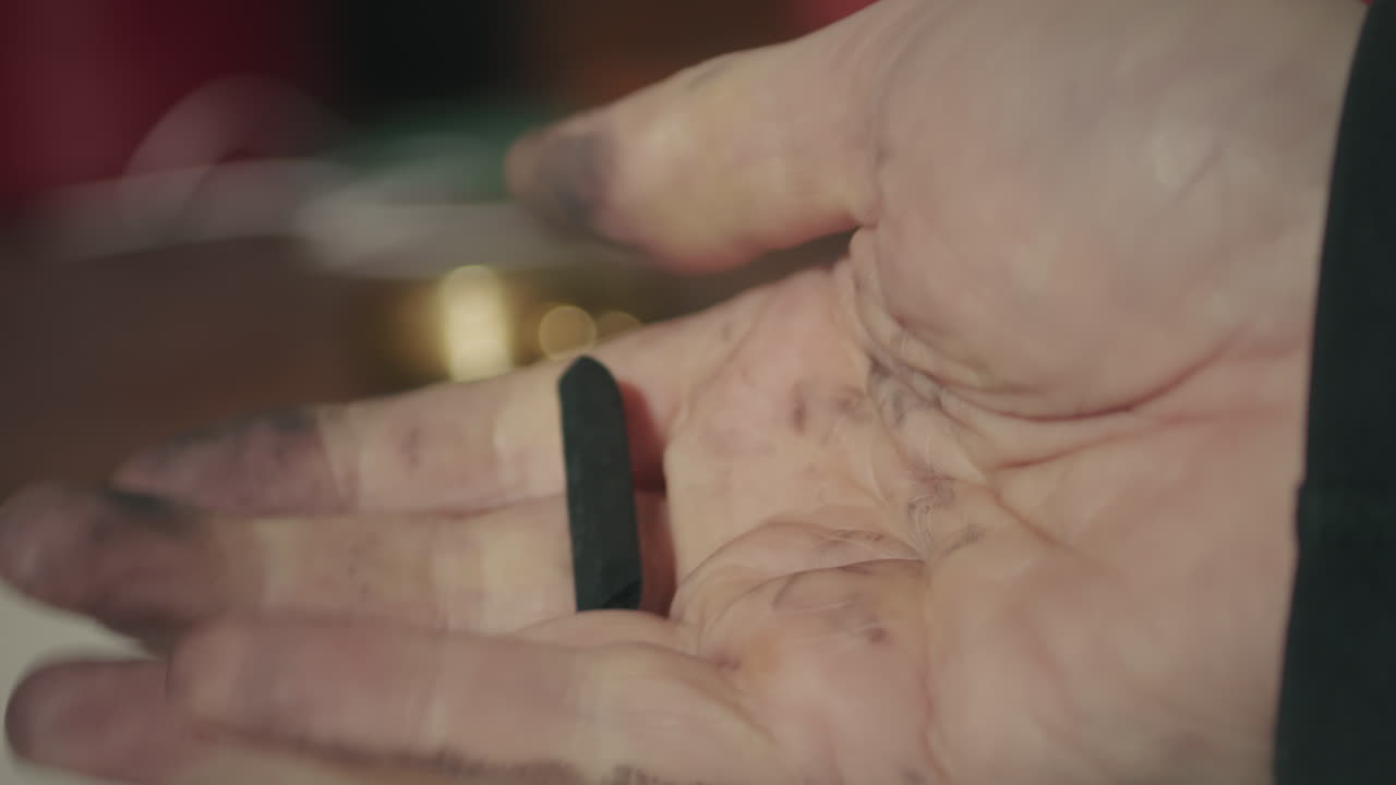 Primo piano macro della mano di un artista macchiata di carboncino, che fa rotolare un pastello a cera in un momento di contemplazione e immersione creativa.