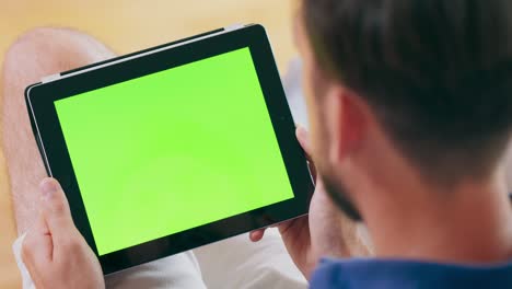 un hombre toma una llamada de video en una computadora tablet, que cuenta con una pantalla verde