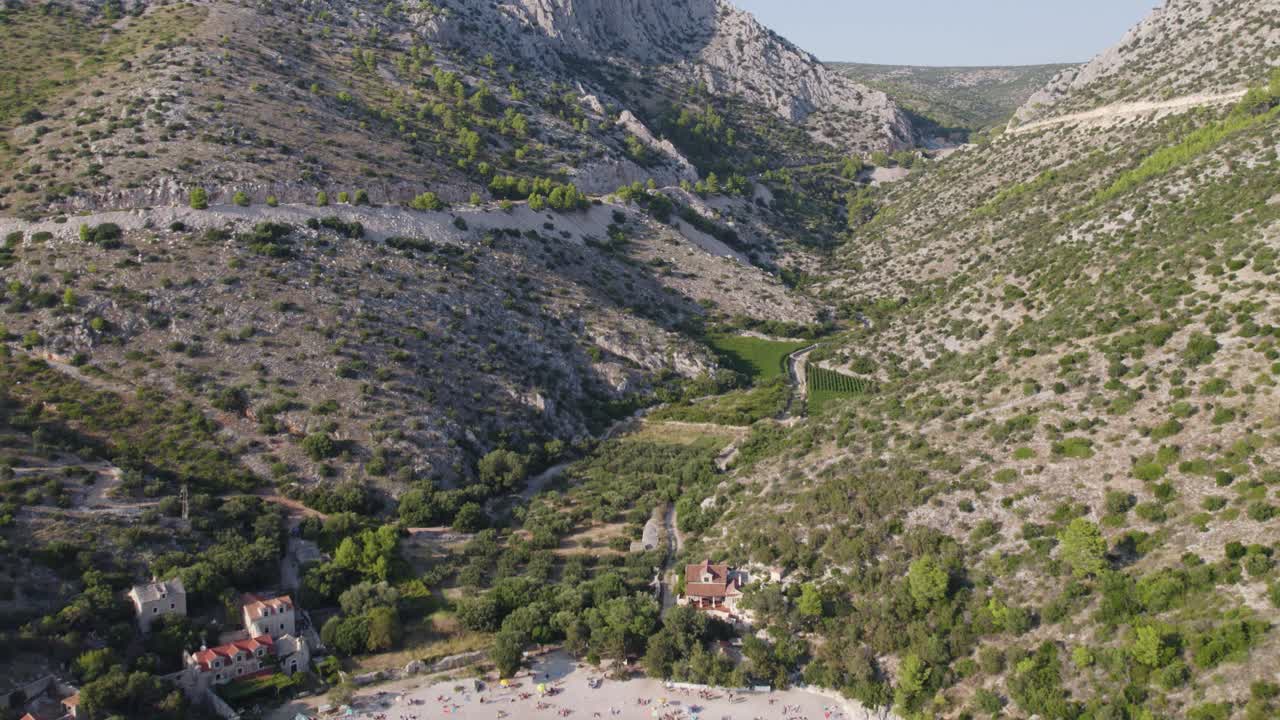 Un drone si allontana da una profonda valle verde per rivelare la spiaggia di Dubovica sull'isola di Hvar, Croazia.