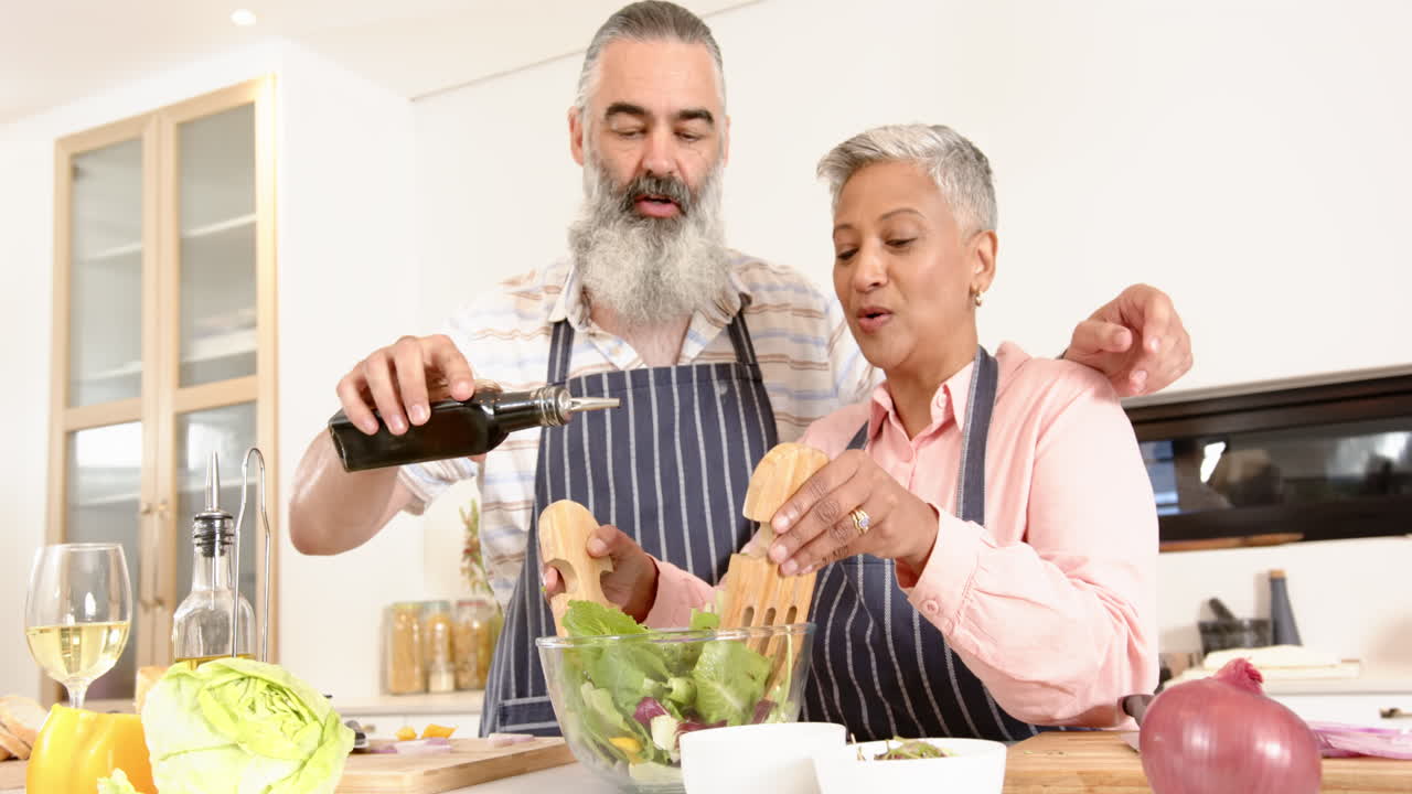 Senior couple preparing salad together, pouring olive oil and mixing ingredients