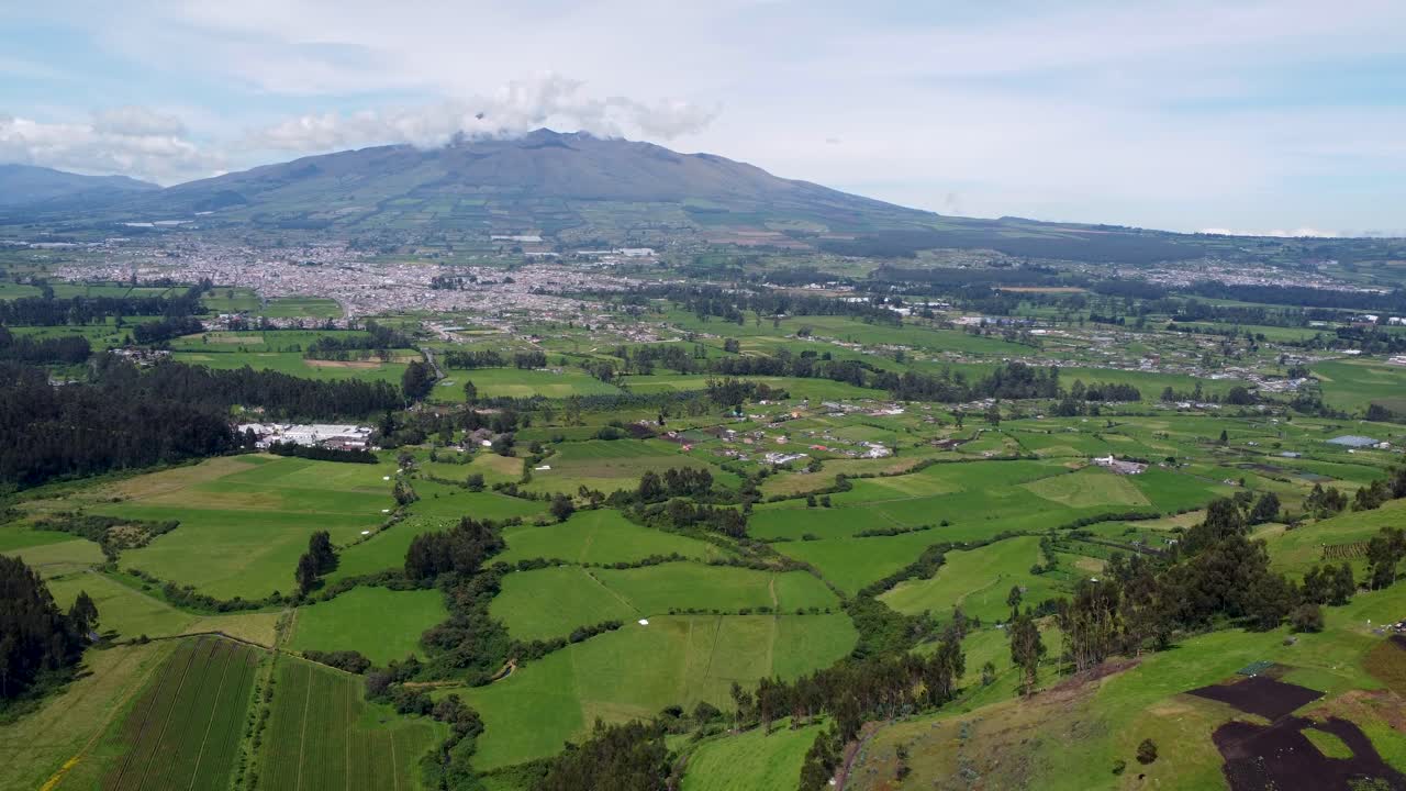 Clip cinematografica con drone che si muove sui campi verdi verso una piccola città sotto una montagna a Puichig, Ecuador.