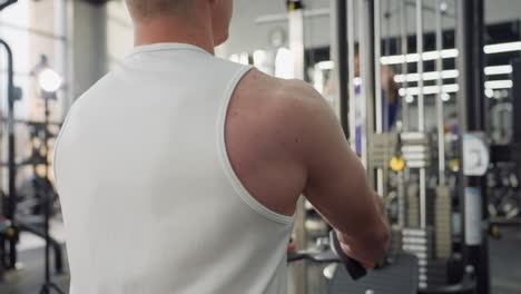 back view of fit athlete on chest press machine pushing handles against weight stack with focused form in busy gym setting surrounded by other exercisers and equipment showcasing upper body workout