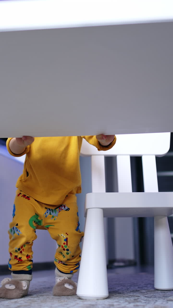 Cute smiling kid squatting near the desk. Playful cheerful baby boy in his room. Vertical video