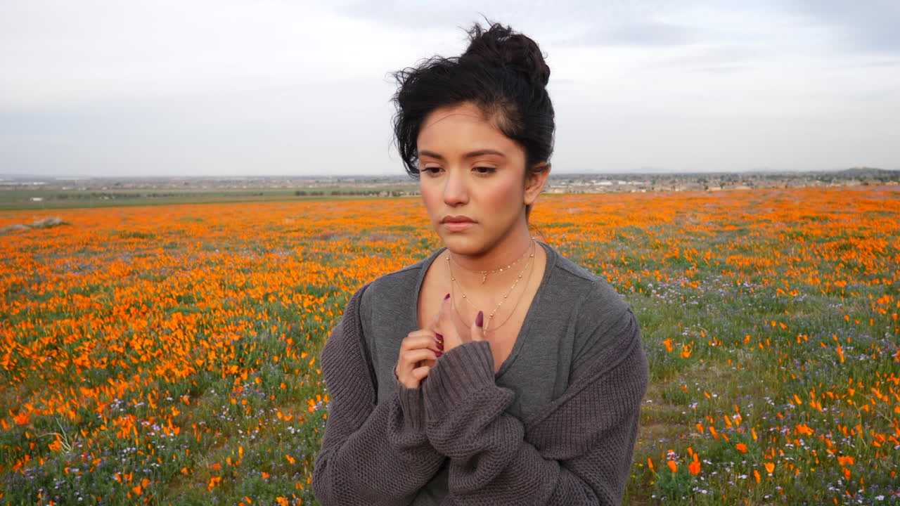 una hermosa mujer joven mostrando emociones tristes y afligidas en su cara en un campo de flores silvestres en la naturaleza en cámara lenta