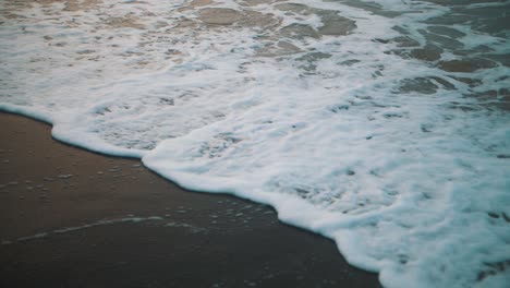 close-up shot of the foam of a wave crashing on the shore of the beach in slow motion