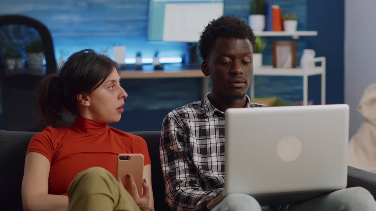 Modern interracial couple using technology on couch