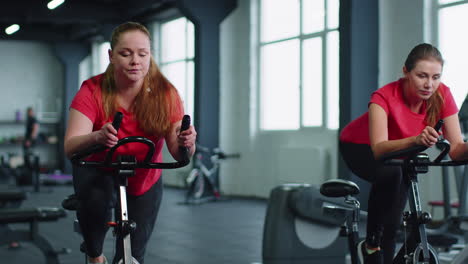 Group-of-smiling-friends-women-class-exercising,-training,-spinning-on-stationary-bike-at-modern-gym