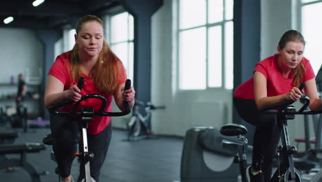 grupo de amigas sonrientes mujeres clase de ejercicio, entrenamiento, girar en bicicleta estacionaria en un gimnasio moderno