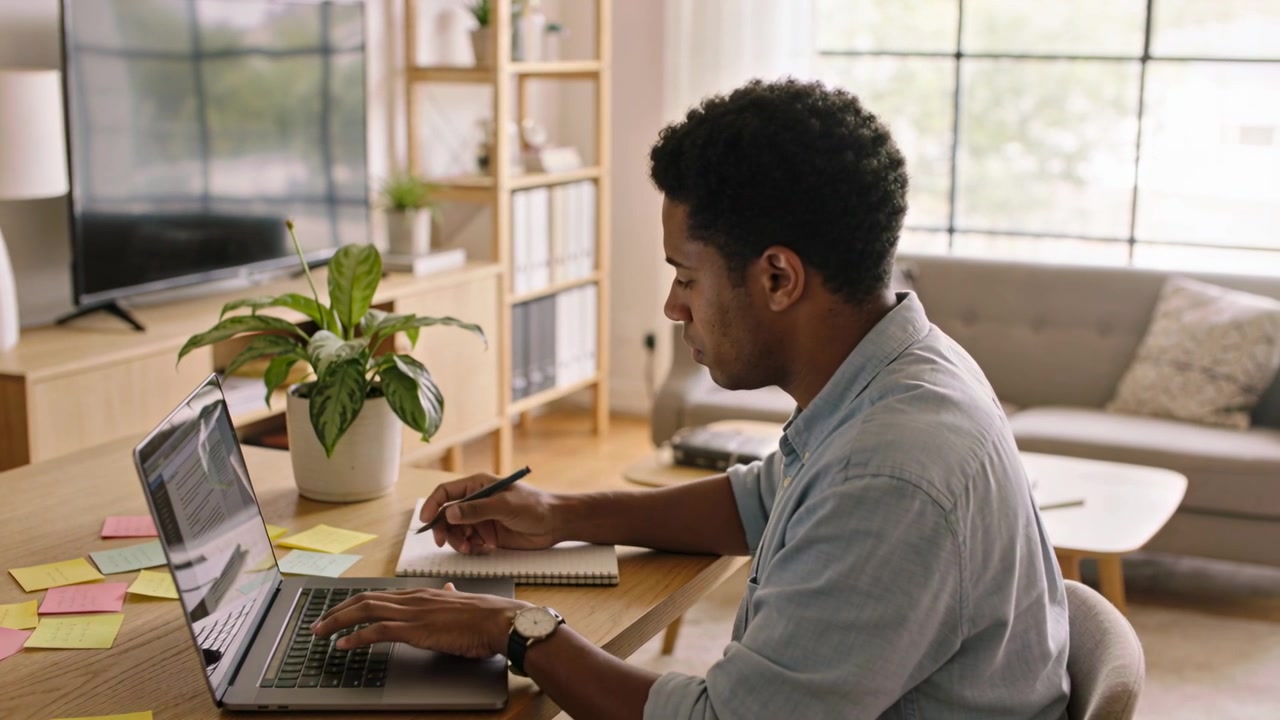 Checking laptop man in shirt working, typing, writing in notebook at home office with sticky-notes