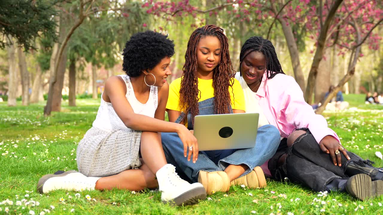 Tre donne sorridenti che usano un portatile al parco