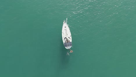 a sailing boat in the sea with people swimming arround it aerial view from above