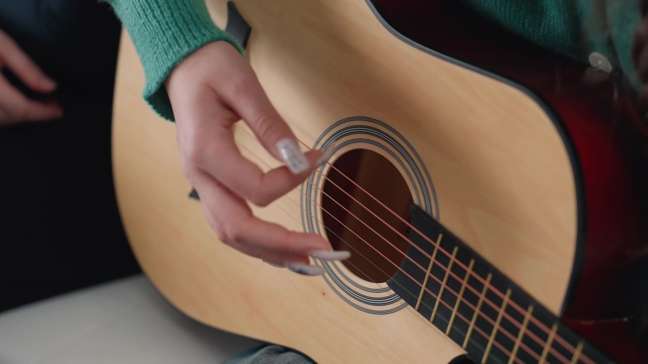 Closeup white hands strumming acoustic guitar with green sweater and pick, precise plucking across steel strings, wood rosette detail, soft natural light, focused practice session in new apartment