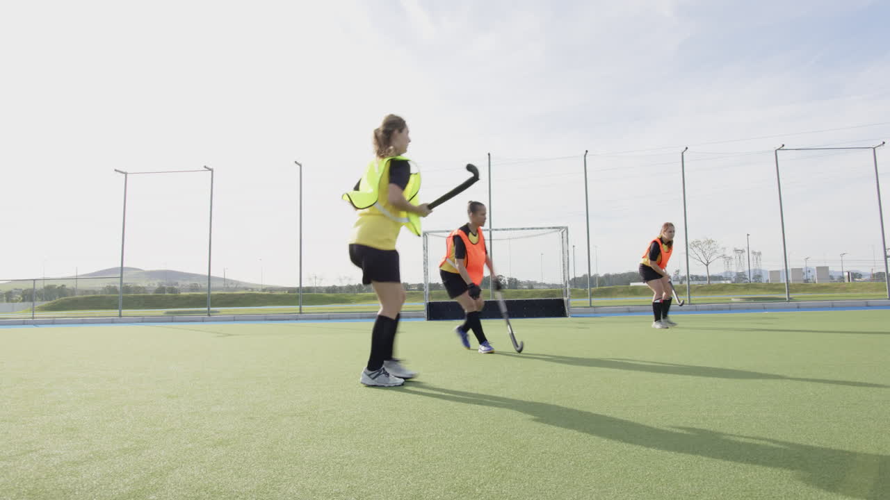 Female hockey players practicing on field, running towards goal with determination