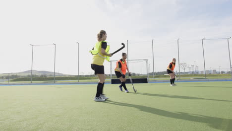 female hockey players practicing on field, running towards goal with determination