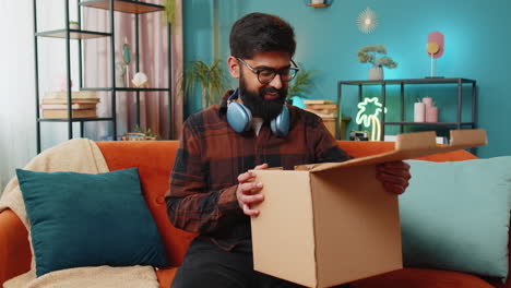 hombre indio feliz comprador desempaquetando caja de cartón entrega paquete compras en línea compra en casa