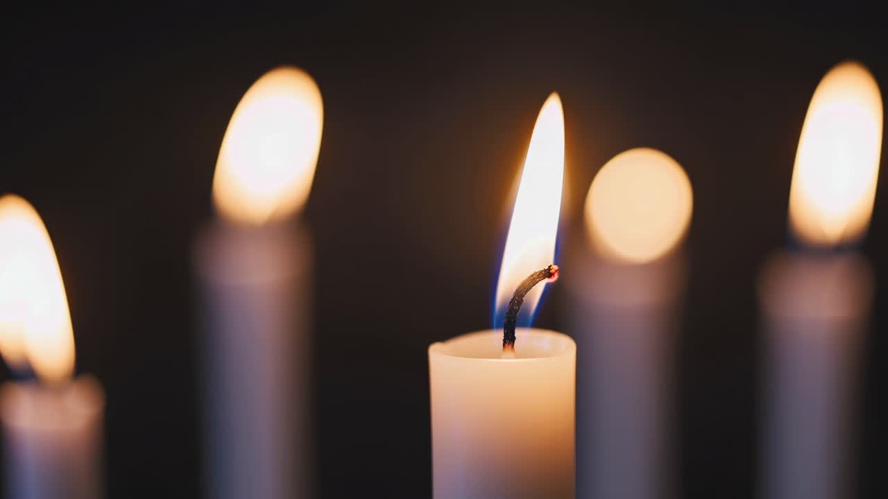 Video ravvicinato di candele accese in condizioni di scarsa illuminazione, con messa a fuoco sulle fiamme tremolanti