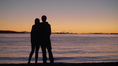 Paar-Silhouette-Am-Strand-Bei-Schönem-Sonnenuntergang-Mit-Entenschwarm-Im-Hintergrund