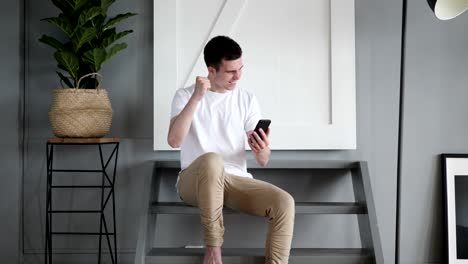 man excited by success using smartphone, sitting on stairs