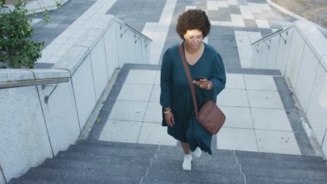 Plus-size-biracial-woman-walking-on-stairs-with-smartphone-in-city