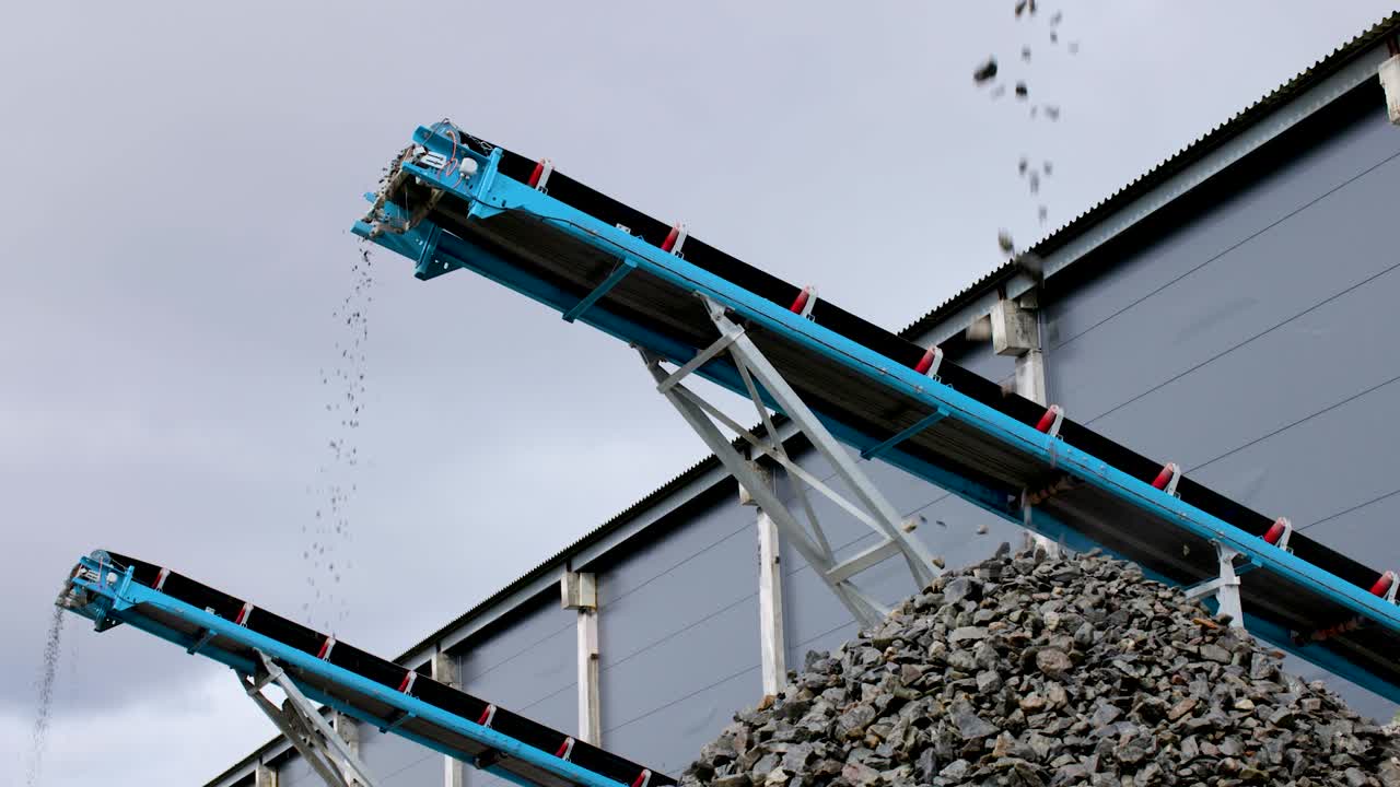 Rocks from a processing plant falls from conveyor belts. Static shot from low angle.
