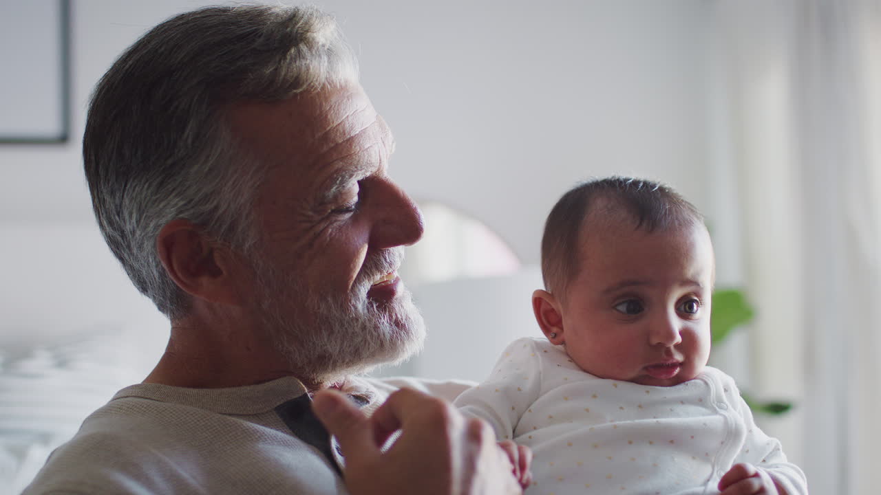 Spansk bedstefar, der holder sit baby-barnebarn, hoved og skuldre, nærbillede.