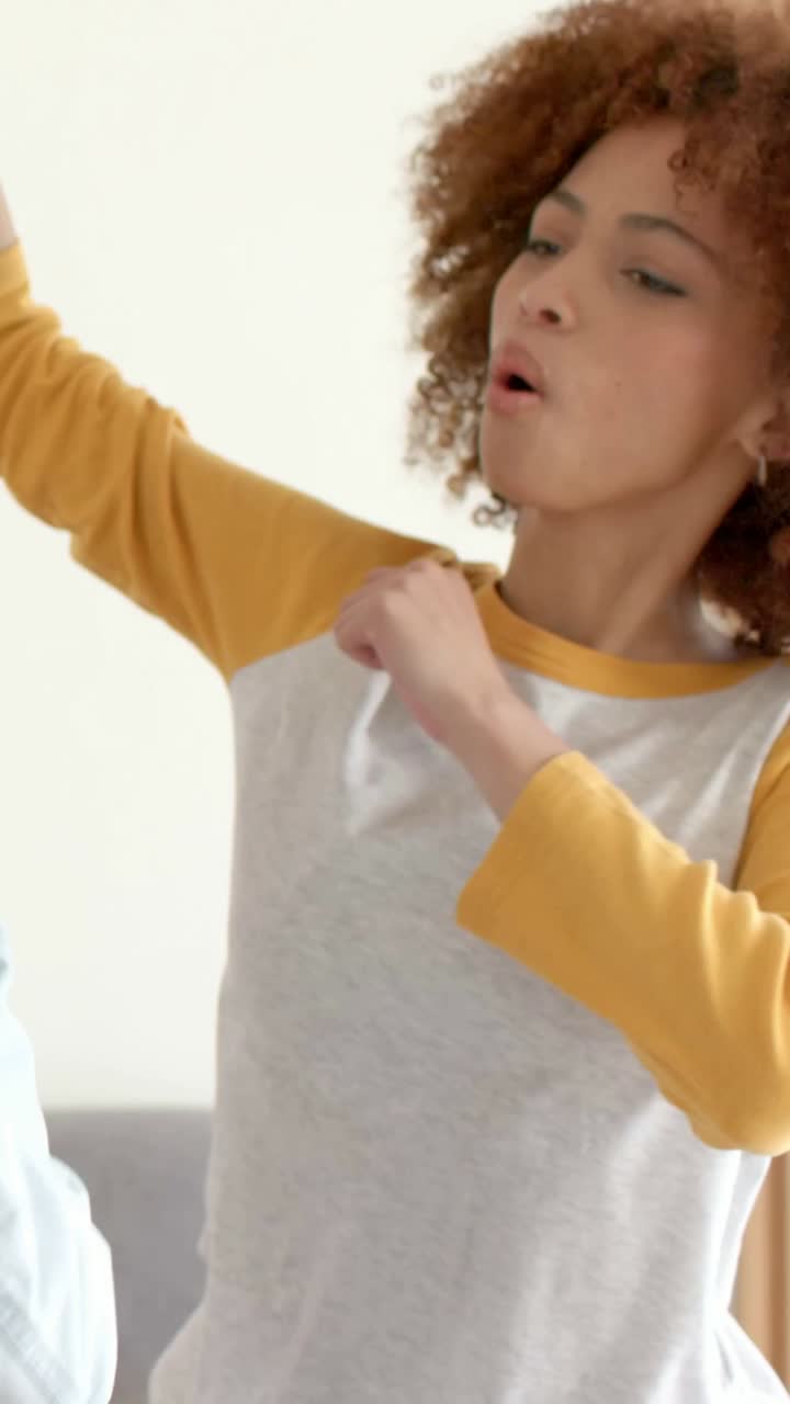 Vertical video: Miming curly woman in raglan singing, dancing and reaching mic at home with friends