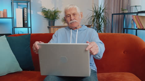 senior grandfather man sitting on sofa closing laptop pc after finishing work in living room at home