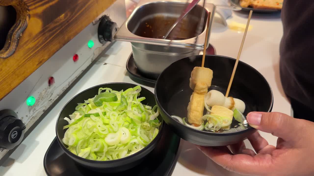 A chef assembles Korean BBQ oden with leeks in a Bangkok restaurant. Warm lighting enhances the inviting culinary atmosphere