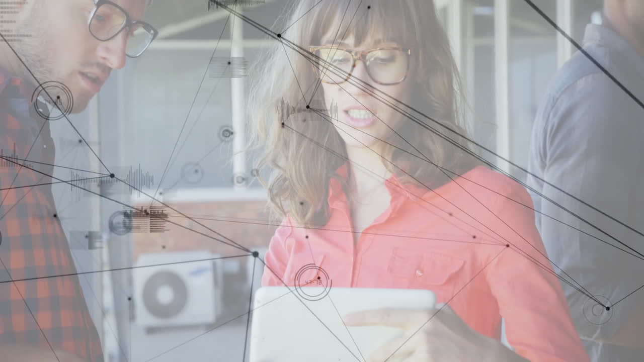 Woman holding tablet speaking with colleagues in tech office, network graphics floating over desk