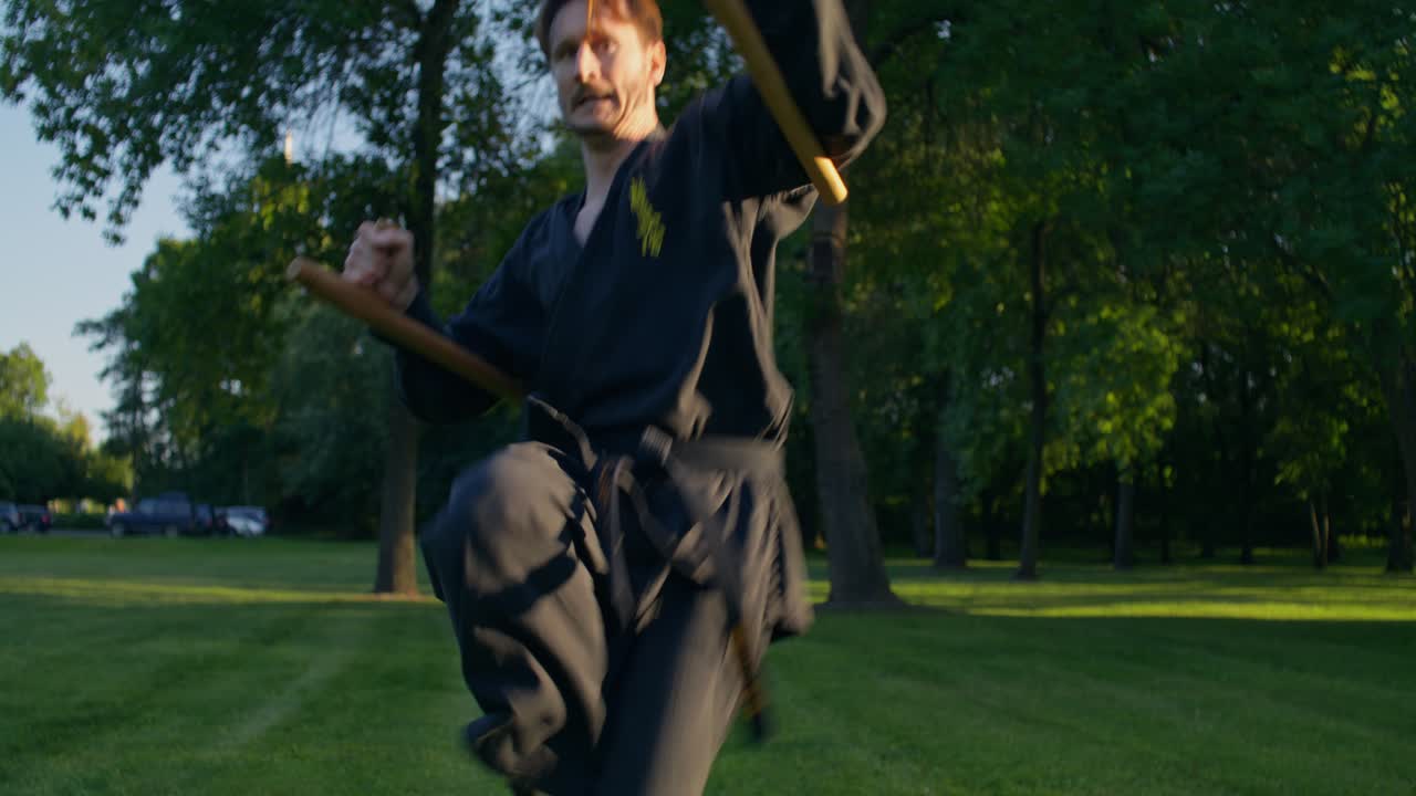 Man practicing martial arts with nunchucks in a park